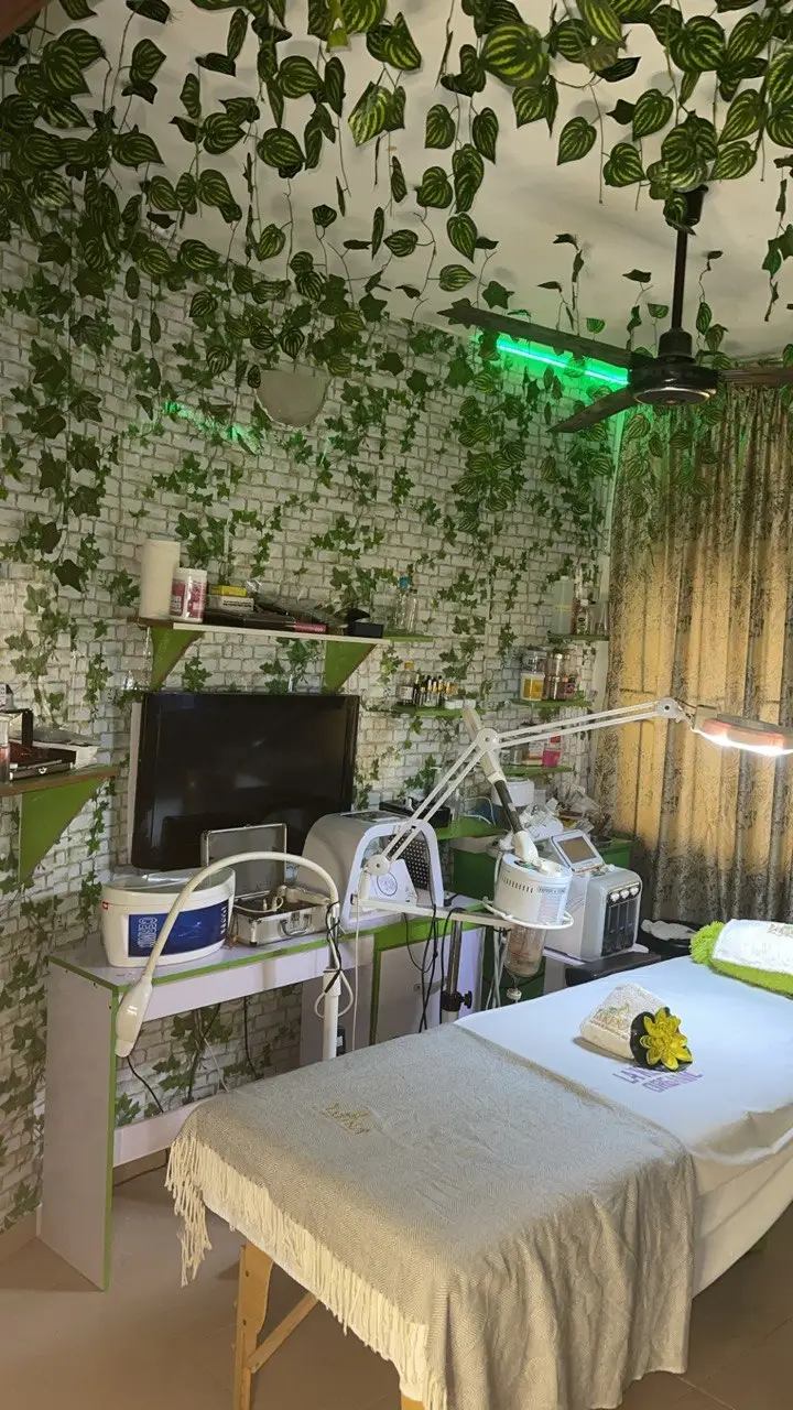 Professional facial treatment room of La'kenzy Skincare & Aesthetic SPA in Mowe, Ogun state featuring a treatment bed, skincare equipment, adjustable magnifying lamp, and botanical wall décor in a serene beauty spa setting.