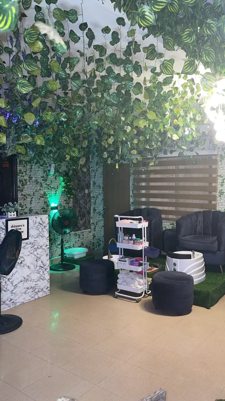 Interior of La'Kenzy Skincare & Aesthetic SPA in Mowe, Ogun state featuring lush hanging greenery, marble reception desk, plush black lounge seating, and professional pedicure equipment in a relaxing treatment environment.
